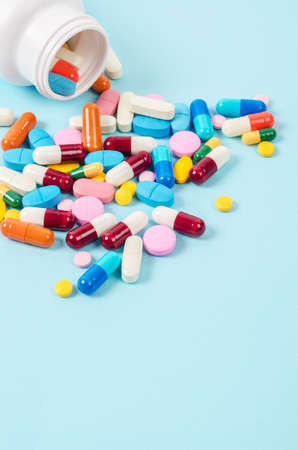 Pills pouring out of the white bottle on blue background.