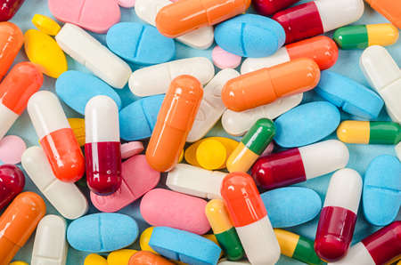 Colorful tablets and capsules pills medicine heap on blue background.