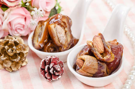 Dried date palm fruits in white spoon on tablecloth.