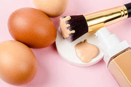 Liquid fluid foundation glass bottle on makeup sponges and egg on pink