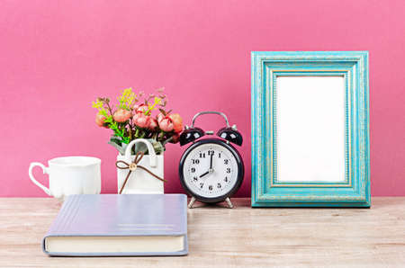 Blank photo frame on desk space with notebook on pinkの写真素材