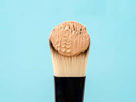 Pouring liquid beige makeup foundation on a brush makeup with blue
