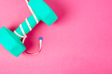 Green dumbbell and measuring tape on pink  with free space for your text or message. Weight Loss concept.の写真素材