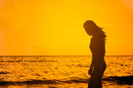 beautiful young slim girl standing on sandy beach at sea at the sunset
