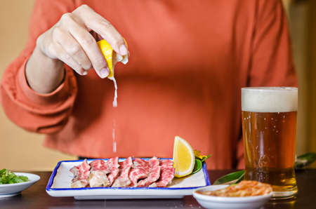 Hands hold lime with lime juice on sliced grilled Strip Loin rare beef steak.の写真素材