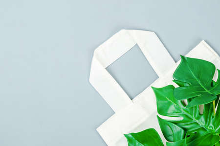 White cotton bag and green leaves on grey background. Mock up for design ecological object concept.