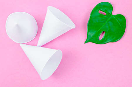 Disposable paper cone water cups with green leaf on pink background.の写真素材