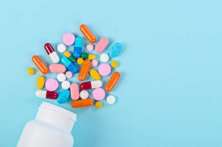 Medical pills and tablets spilling out of a drug bottle on blue background.