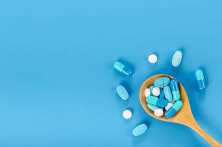 Medicine pill in wooden spoon on blue background.