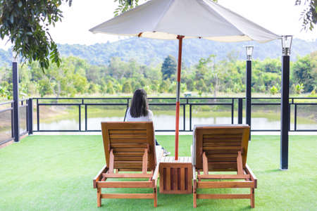 The back of a woman sits on a lone wooden chair among the beautiful natural mountains.