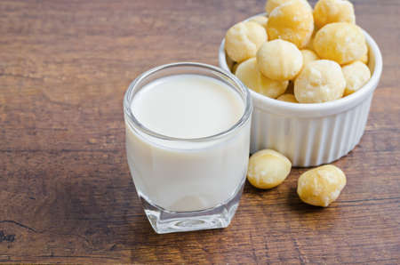 Macadamia milk in a glass and a bowl of macadamia nuts on a wooden background.の写真素材
