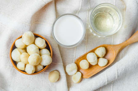 Macadamia milk in a glass and a bowl of macadamia nuts with oil on tablecloth.の写真素材