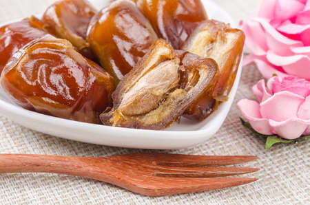 Dried dates fruit in white bowl and wooden fork.
