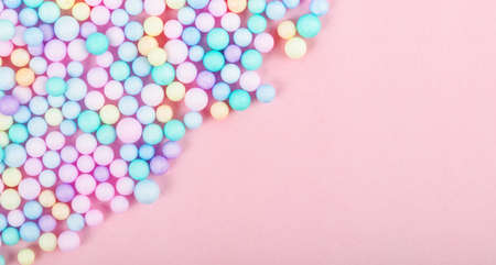 Foam beads of various colors brightly colored on pink pastel background with empty space.の写真素材