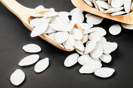 Dried white pumpkin seeds with wooden scoop on black background.の写真素材