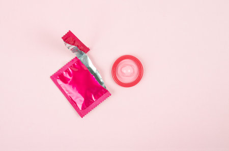 Pink opened condom unpack on a pink background. Safe sex and reproductive health concept.