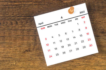 The April 2022 calencar and wooden push pin on wooden background.