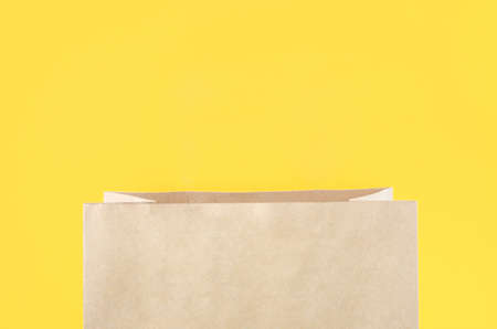 The open brown paper shopping bag on yellow background.