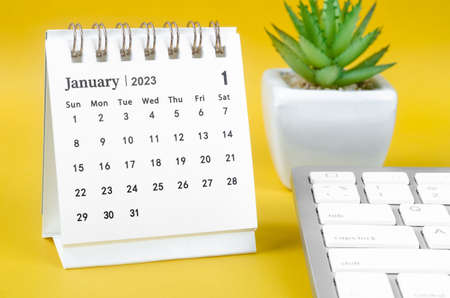 January 2023 desk calendar and computer keyboard on yellow background.