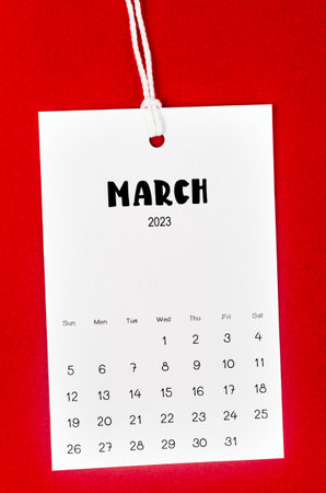 March 2023 calendar page hanged on white rope  on Red background.