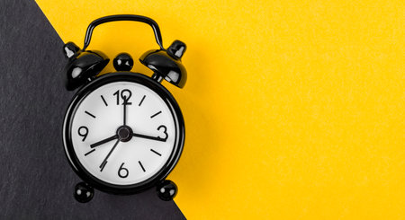 Black vintage alarm clock on yellow background with empty space for your text or message.の写真素材