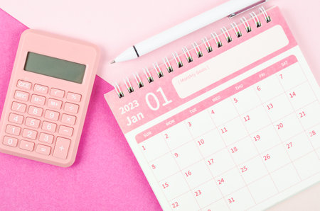 January 2023 desk calendar for 2023 year with calculator and pen on pink color background.の写真素材