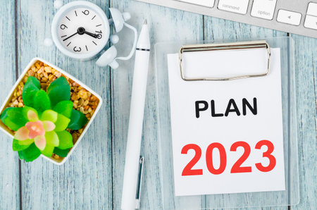Plan 2023 text on clipboard with pen and keyboard computer on wooden background.