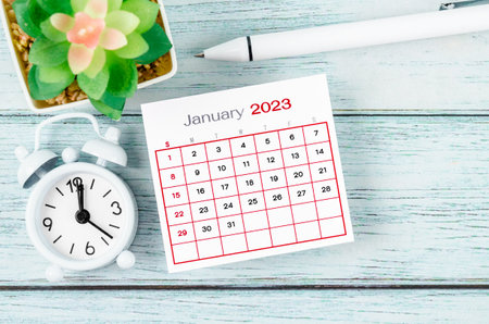 January 2023 Monthly calendar year and alarm clock with pen on blue wooden background.