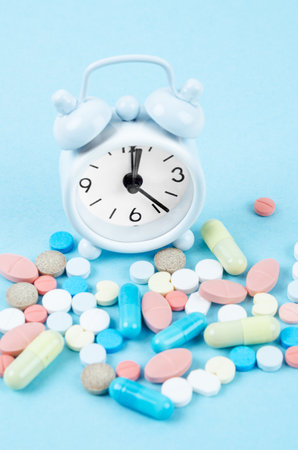 White alarm clock and many drug on a blue background. Taking medicine at the right time concepts.の写真素材