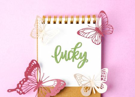 Lucky text on diary and paper butterfly on pink colour background.の写真素材