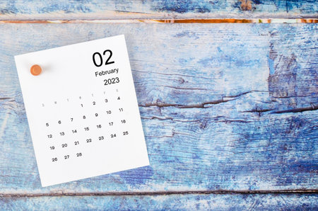 February 2023 monthly calendar and wooden push pin on blue wooden background.の写真素材