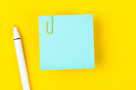 Blank blue notes paper and pen with a paper clip   on yellow background, for your text or message.