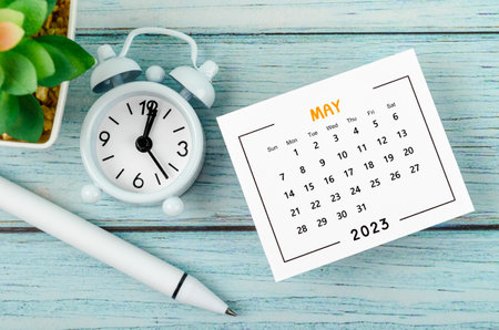 May 2023 Monthly calendar year and alarm clock with pen on blue wooden background.の写真素材