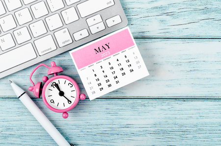 May 2023 Monthly calendar year and alarm clock with keyboard computer on wooden background.