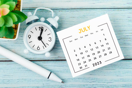 July 2023 Monthly calendar year and alarm clock with pen on blue wooden background.の写真素材