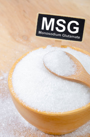 Monosodium glutamate, MSG in wooden spoon on wooden cup with text MSG.