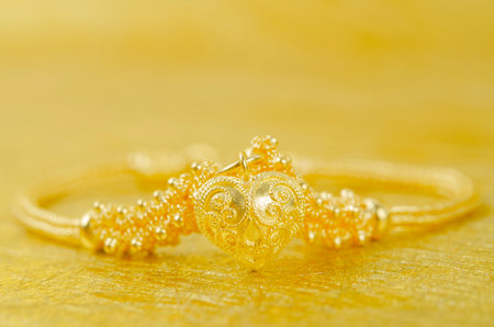 Gold bracelet and heart shape pendant on gold color background.の写真素材
