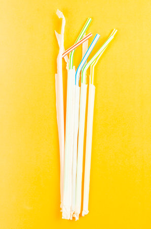 Plastic drinking straws with paper package on yellow background. Garbage concept.の写真素材
