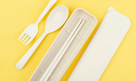 Plastic spoons, forks and chopsticks set on yellow background.の写真素材