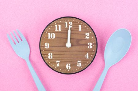 Wooden clock with cutlery on pink color background. Concept of intermittent fasting, lunchtime, diet...