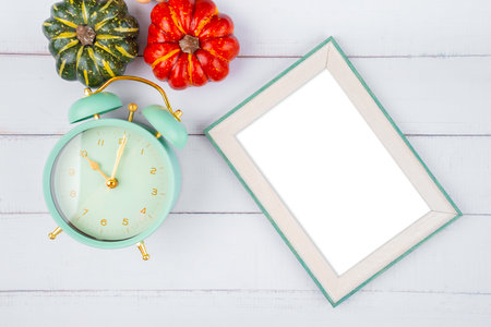 Top view of blank photo frame and vintage alarm clock with pumpkin on wooden background, Save clipping path.の写真素材