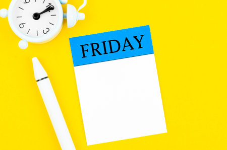 Blank note paper for Friday and pen with alarm clock on yellow background for your text or message.の写真素材