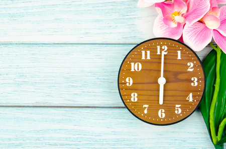 Wooden Alarm clock and pink streaked orchid flower on blue wooden background.