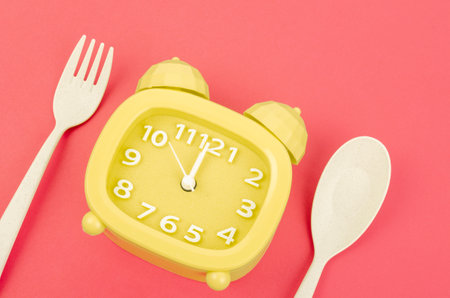 Yellow alarm clock with cutlery on red color background. Concept of intermittent fasting, lunchtime, diet and weight lossの写真素材