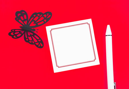 Blank reminder note paper and carve of paper butterfly with pen on red background, space for text.の写真素材