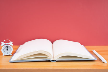 Open blank notebook and pen with alarm clock on the table.の写真素材