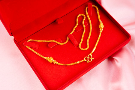 Gold necklace in a red box on a pink fabric background.の写真素材