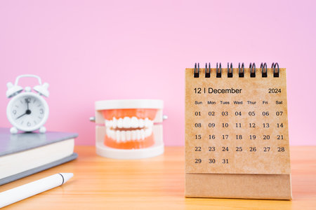 December monthly desk calendar for 2024 year and model dentures on the table with alarm clock. Dental health concepts.の写真素材
