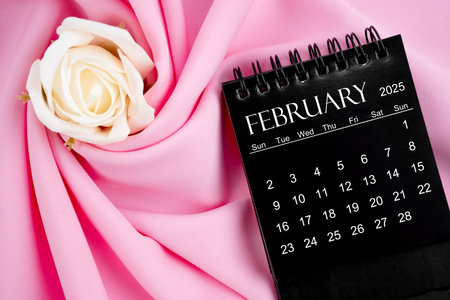 February 2025 desk calendar black color and rose on pink textile background.の写真素材