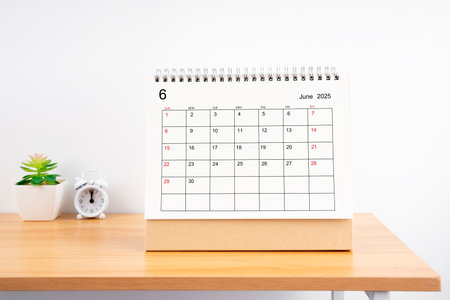 June 2025, Monthly desk calendar for 2025 year on wooden table with alarm clock.の写真素材